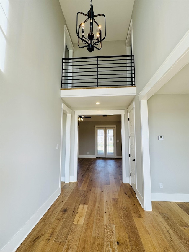 hall with light hardwood / wood-style floors, french doors, a chandelier, and a high ceiling