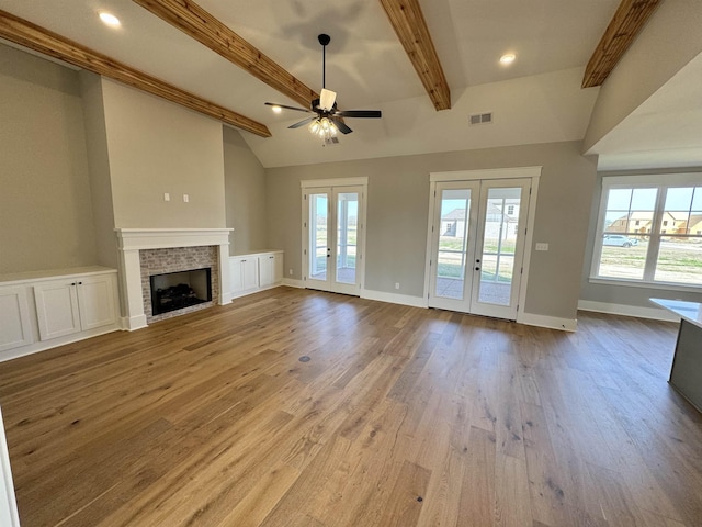 unfurnished living room featuring ceiling fan, light hardwood / wood-style flooring, french doors, and lofted ceiling with beams