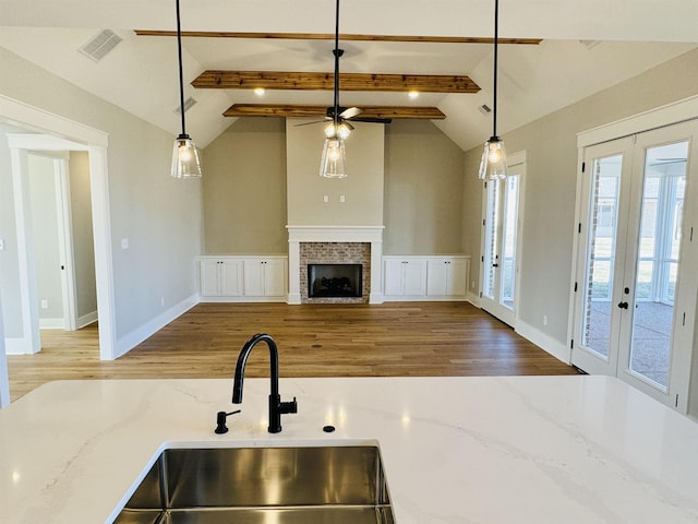 kitchen with light stone counters, french doors, lofted ceiling with beams, and pendant lighting