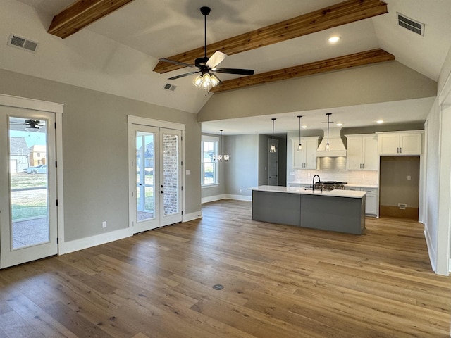 kitchen featuring decorative light fixtures, white cabinetry, light hardwood / wood-style flooring, premium range hood, and a kitchen island with sink