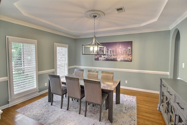 dining area featuring a notable chandelier, a tray ceiling, light hardwood / wood-style flooring, and ornamental molding