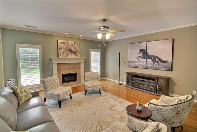 living room with a tile fireplace, ceiling fan, crown molding, and hardwood / wood-style floors