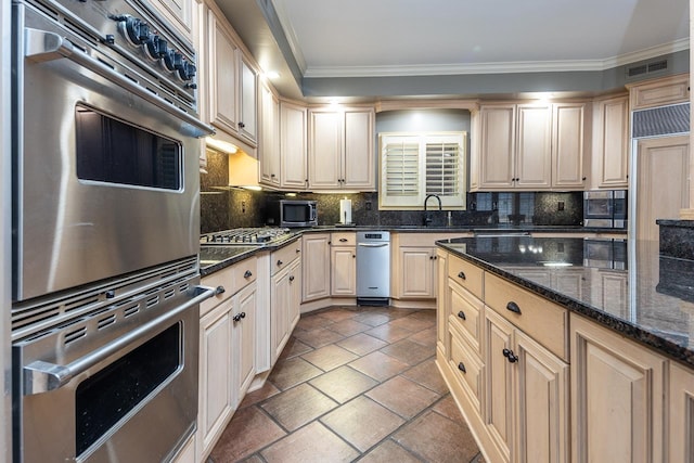 kitchen featuring backsplash, crown molding, appliances with stainless steel finishes, dark stone countertops, and sink