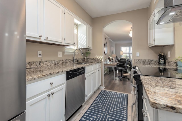 kitchen featuring white cabinets, stainless steel appliances, light stone counters, sink, and extractor fan