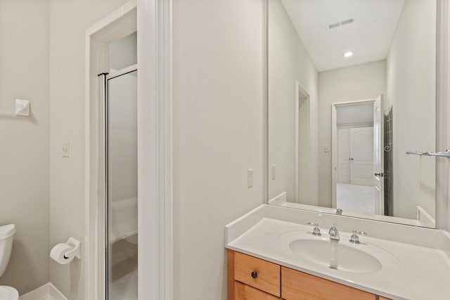 bathroom with toilet, vanity, and a shower with shower door