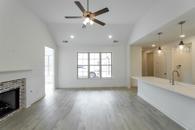 unfurnished living room featuring vaulted ceiling, light hardwood / wood-style floors, ceiling fan, a fireplace, and sink