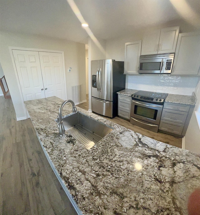 kitchen featuring light stone counters, backsplash, dark hardwood / wood-style flooring, appliances with stainless steel finishes, and sink