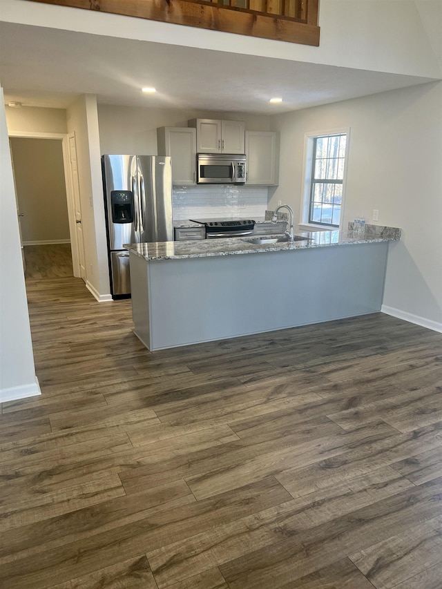 kitchen with gray cabinetry, stainless steel appliances, kitchen peninsula, light stone counters, and tasteful backsplash