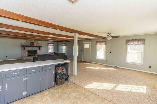 kitchen featuring beamed ceiling, a fireplace, ceiling fan, and a wealth of natural light