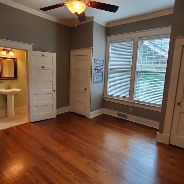 unfurnished bedroom with ceiling fan, dark wood-type flooring, ornamental molding, sink, and ensuite bathroom