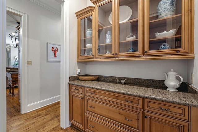 bar featuring ornamental molding, light wood-type flooring, and dark stone countertops