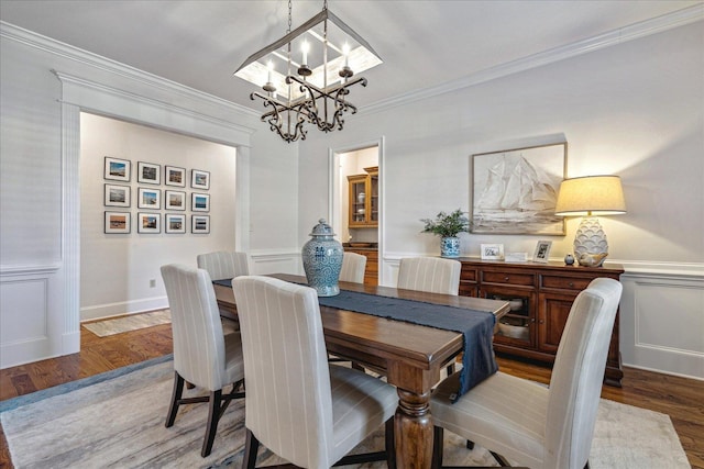 dining area with wood-type flooring, ornamental molding, and a notable chandelier