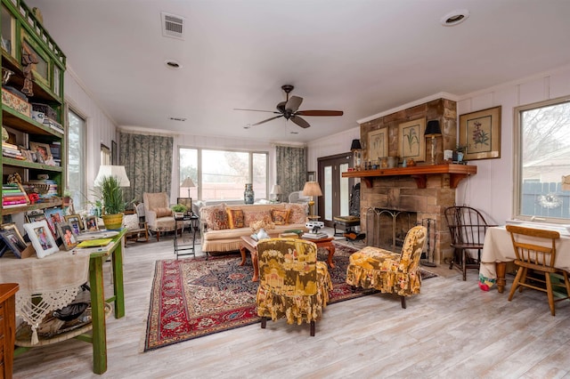 living room with ceiling fan, a wealth of natural light, ornamental molding, and a stone fireplace