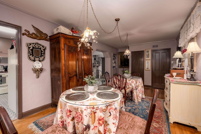 dining space featuring a chandelier, light wood-type flooring, and ornamental molding