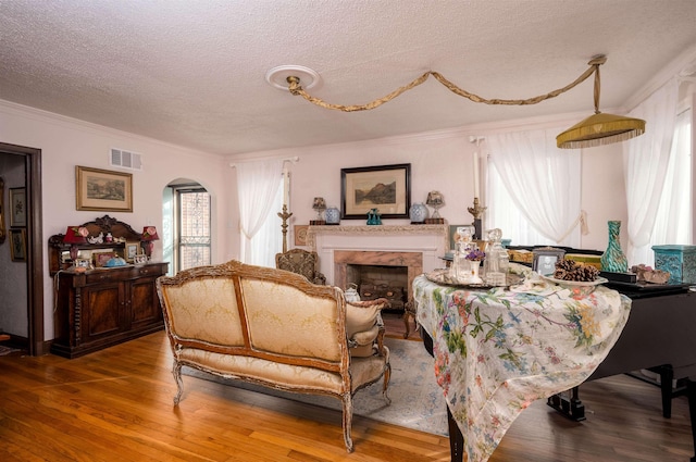 living room with a textured ceiling, ornamental molding, a fireplace, and wood-type flooring