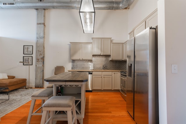 kitchen featuring a high ceiling, stainless steel appliances, light wood-type flooring, sink, and tasteful backsplash