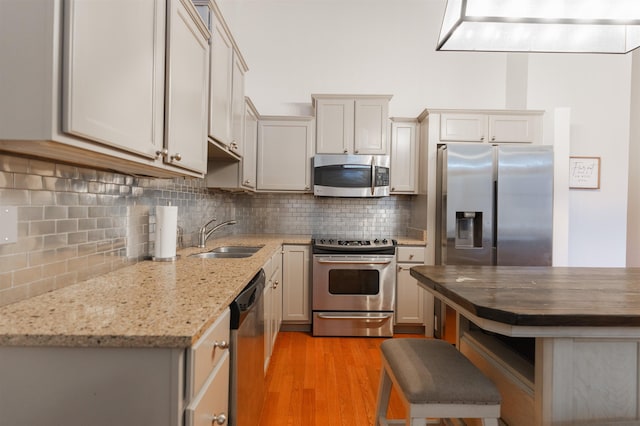 kitchen with stainless steel appliances, light wood-type flooring, light stone counters, decorative backsplash, and sink