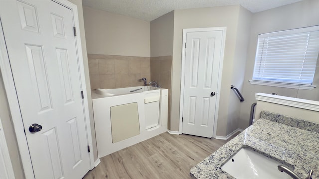 bathroom with a textured ceiling, a tub to relax in, hardwood / wood-style flooring, and vanity