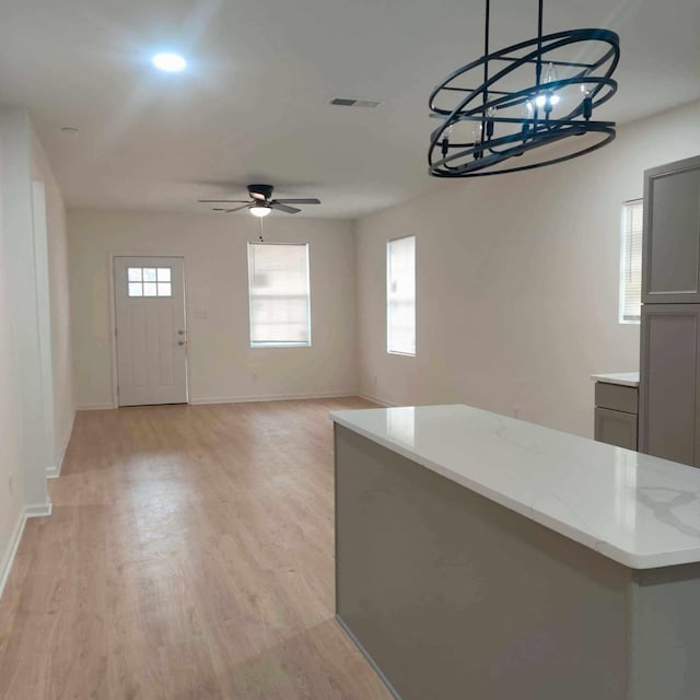 kitchen featuring decorative light fixtures, light stone counters, light hardwood / wood-style floors, ceiling fan with notable chandelier, and gray cabinets