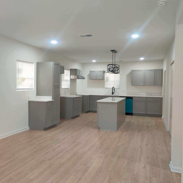 kitchen featuring a center island, light hardwood / wood-style floors, wall chimney range hood, pendant lighting, and gray cabinetry