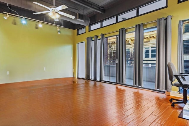 empty room with a towering ceiling, wood-type flooring, rail lighting, and ceiling fan