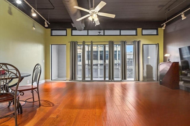 interior space with ceiling fan, hardwood / wood-style floors, a towering ceiling, and rail lighting