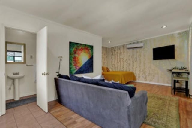 living room with crown molding, a wall mounted air conditioner, wood-type flooring, and sink