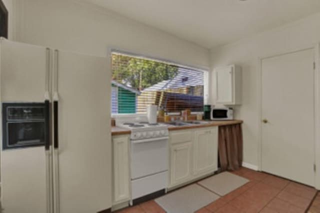 kitchen featuring white appliances, light tile patterned floors, and white cabinetry