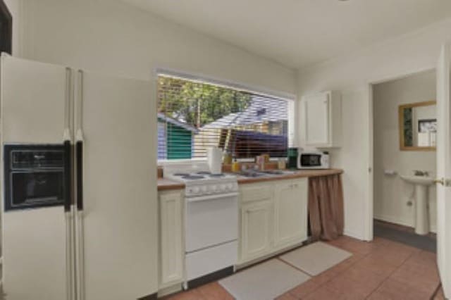 kitchen with sink, white appliances, white cabinetry, and light tile patterned floors