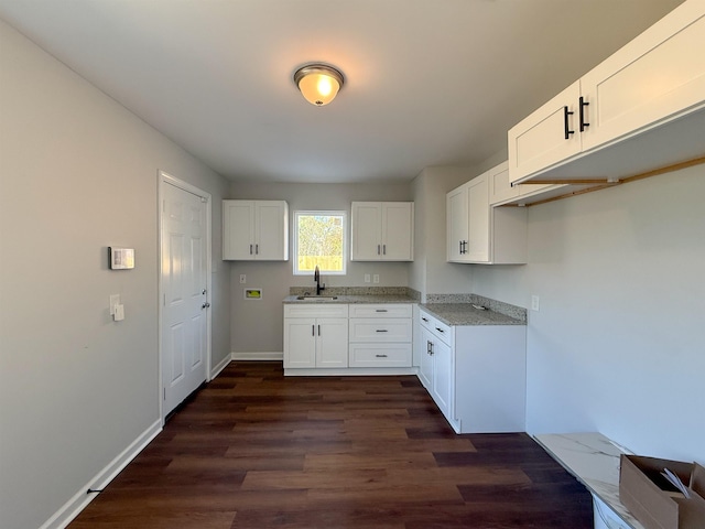 kitchen with sink, dark wood-type flooring, white cabinetry, and light stone countertops