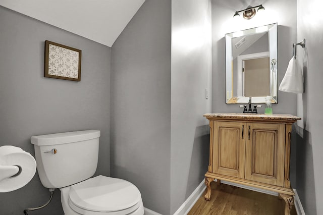 bathroom featuring toilet, hardwood / wood-style flooring, vaulted ceiling, and vanity