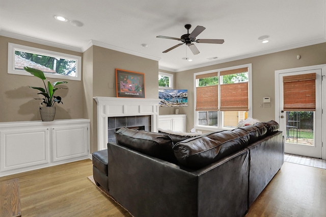 living room with crown molding, a tiled fireplace, ceiling fan, and light hardwood / wood-style flooring