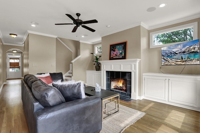 living room with a tile fireplace, hardwood / wood-style floors, ceiling fan, and crown molding