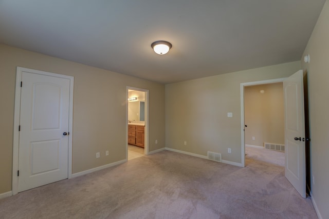 unfurnished bedroom featuring light colored carpet and connected bathroom