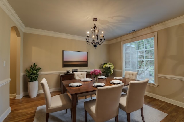 dining space with an inviting chandelier, ornamental molding, and dark wood-type flooring