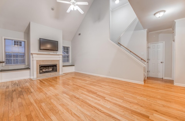 unfurnished living room featuring crown molding, ceiling fan, high vaulted ceiling, a fireplace, and light hardwood / wood-style flooring