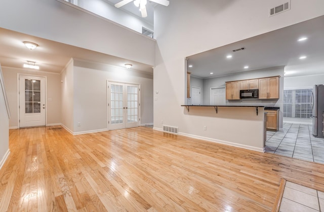 unfurnished living room featuring a towering ceiling, ceiling fan, french doors, and light hardwood / wood-style floors