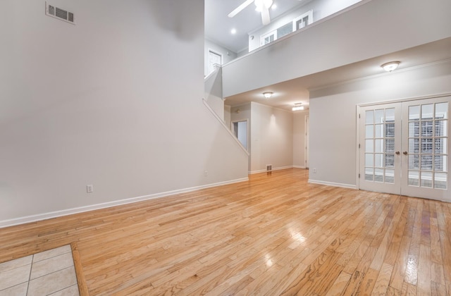 unfurnished living room featuring a towering ceiling, ceiling fan, french doors, and light hardwood / wood-style floors