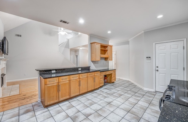 kitchen featuring kitchen peninsula, light tile patterned floors, dark stone countertops, crown molding, and ceiling fan