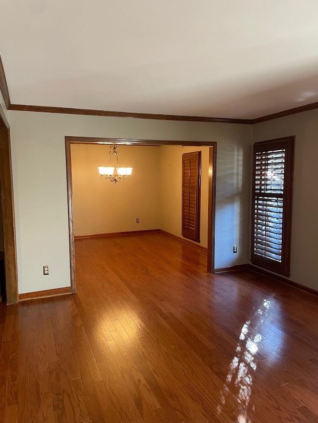 unfurnished room featuring an inviting chandelier, hardwood / wood-style flooring, and crown molding