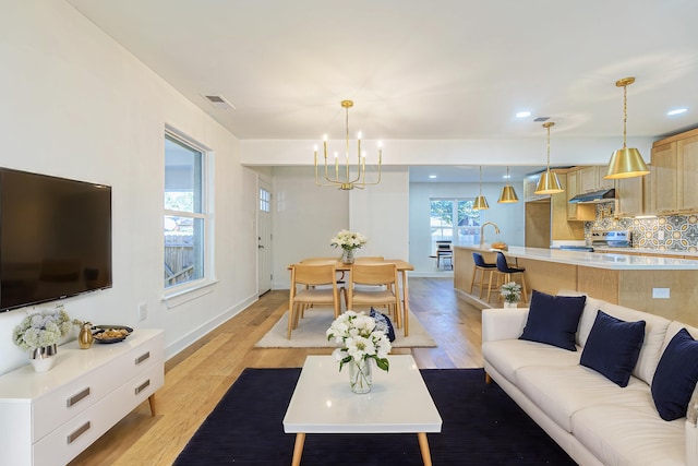 living room with a notable chandelier, light hardwood / wood-style flooring, and sink