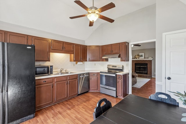 kitchen featuring light hardwood / wood-style floors, stainless steel appliances, a brick fireplace, sink, and tasteful backsplash