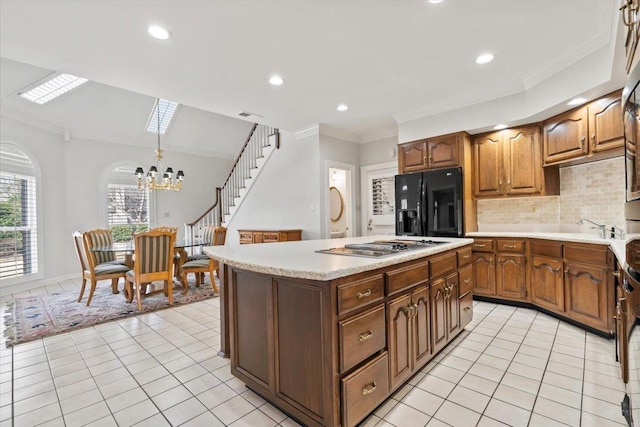 kitchen with black fridge with ice dispenser, decorative backsplash, hanging light fixtures, a kitchen island, and a chandelier