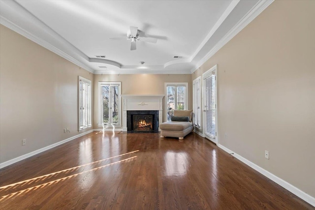 unfurnished living room featuring a raised ceiling, ceiling fan, ornamental molding, and dark hardwood / wood-style floors