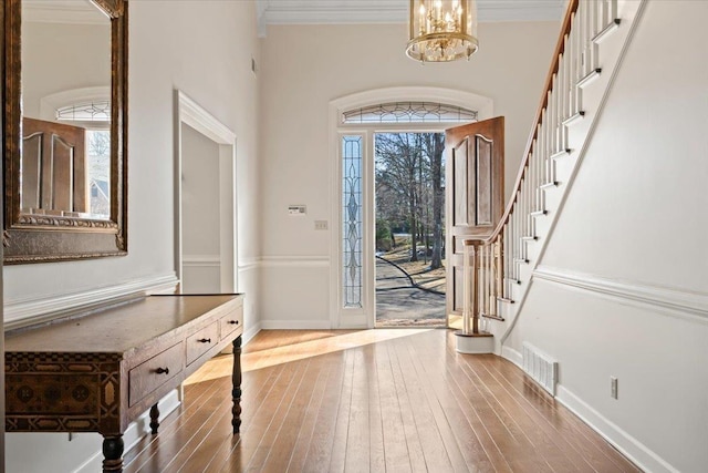 foyer with an inviting chandelier, crown molding, and hardwood / wood-style flooring