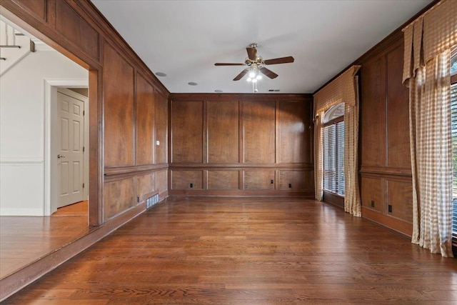 spare room with hardwood / wood-style flooring, wood walls, and ceiling fan