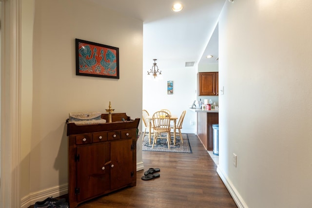 hallway with an inviting chandelier and dark wood-type flooring