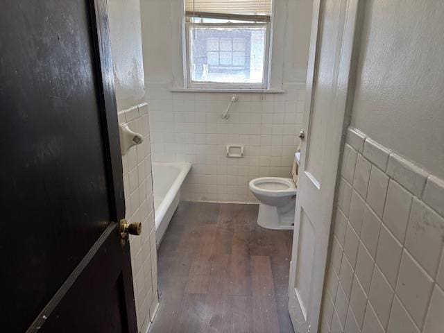 bathroom featuring tile walls, hardwood / wood-style floors, a washtub, and toilet