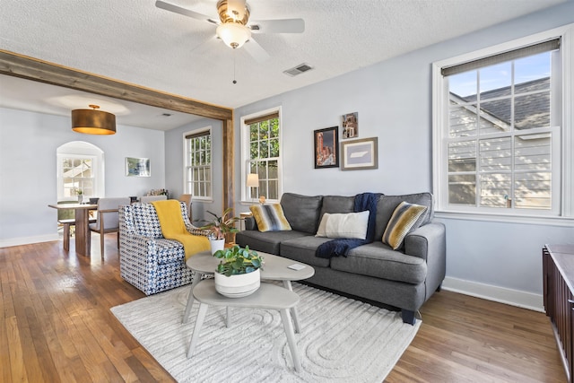 living room featuring ceiling fan, a textured ceiling, beamed ceiling, and wood-type flooring