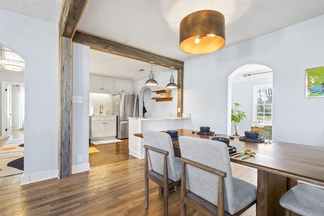 dining room featuring sink, dark wood-type flooring, a textured ceiling, and beamed ceiling